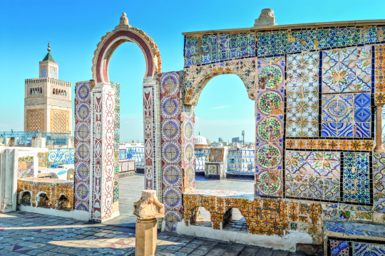 Blick durch alte Bögen mit bunten Fließen in blau, weiß, türkis, im Hintergrund eine Stadt zu erkennen
